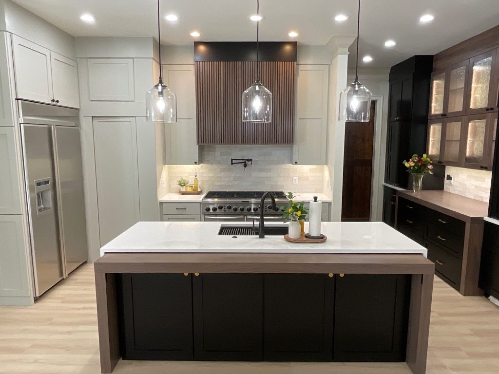 A remodeled kitchen with a large island, quartz countertops, glass pendant lights, wood-accented range hood, and modern two-tone cabinetry.