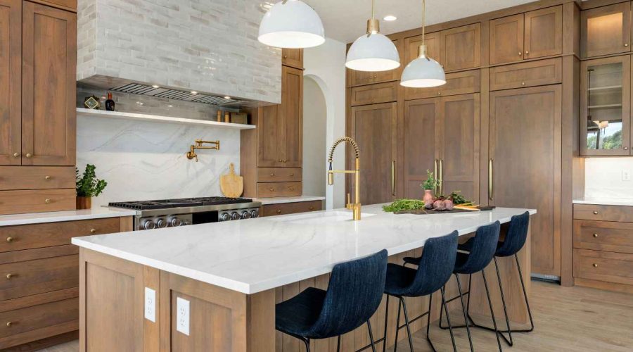 A modern kitchen features light-brown cabinets, a white quartz countertop, and navy blue bar stools.
