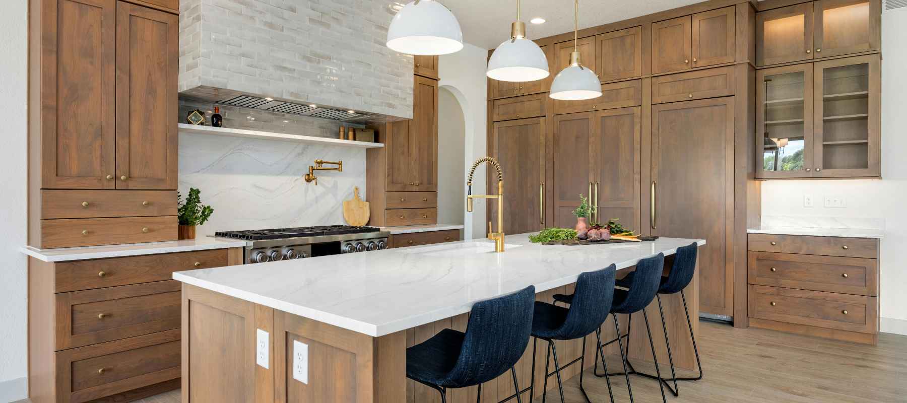 A modern kitchen features light-brown cabinets, a white quartz countertop, and navy blue bar stools.