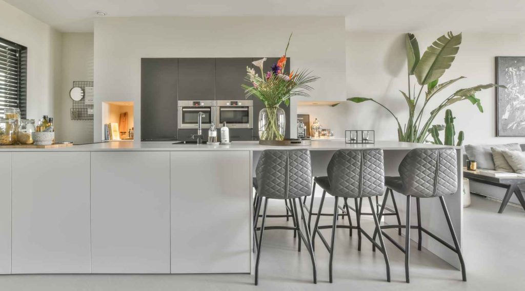 A modern kitchen interior showcases a large, white island with gray bar stools.